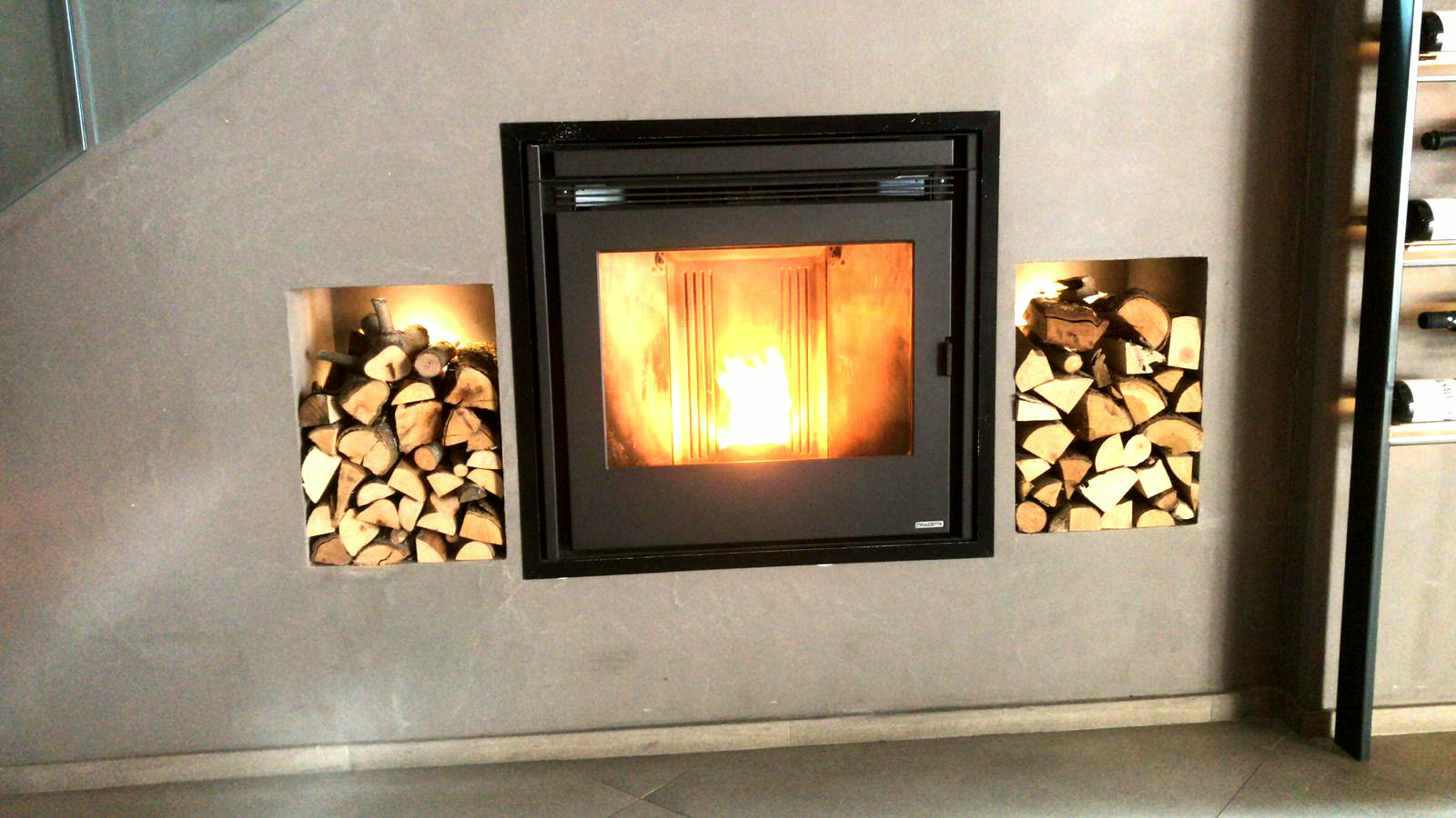 Inserto a pellet incassato in una parete in micro-cemento grigio, con due nicchie laterali per la legna